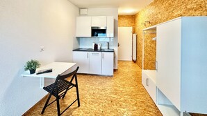Une cuisine compacte avec des meubles blancs, un four encastré et un four à micro-ondes. Il y a un petit coin repas avec une table et une chaise.