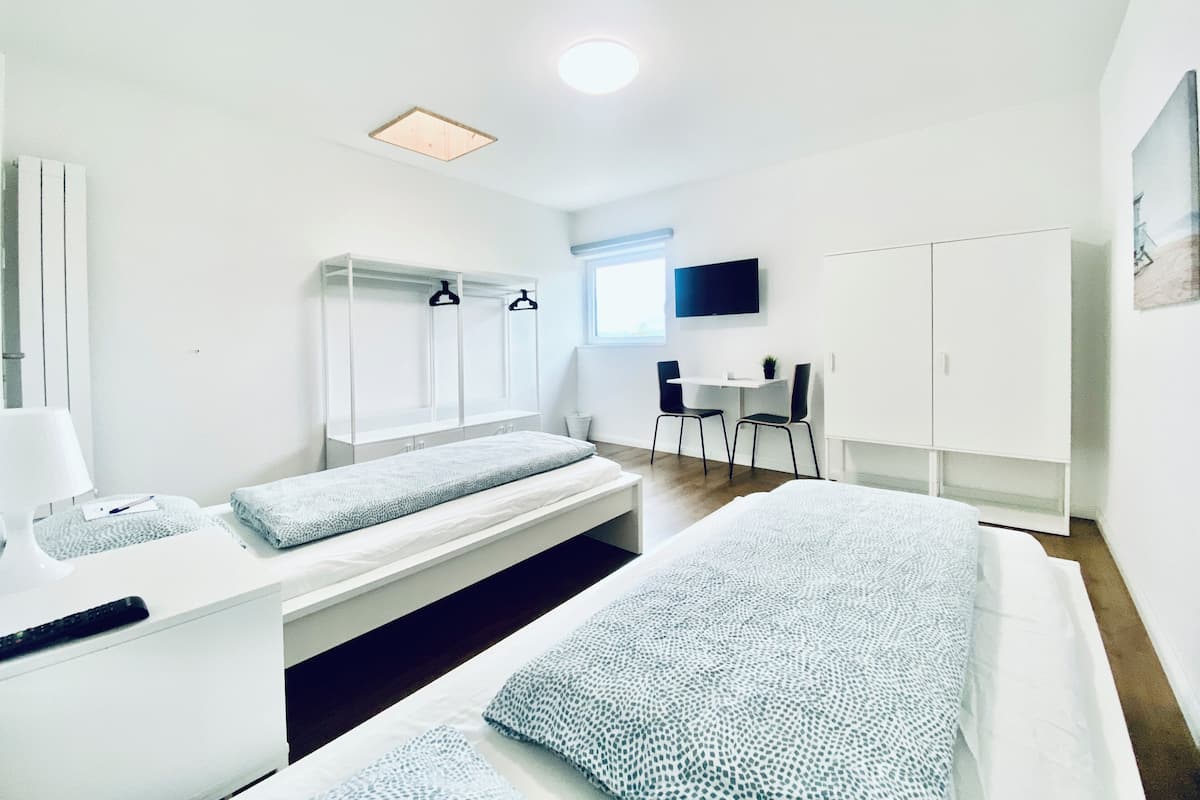 Une chambre à coucher moderne et bien éclairée, avec un lit, un bureau et un téléviseur.