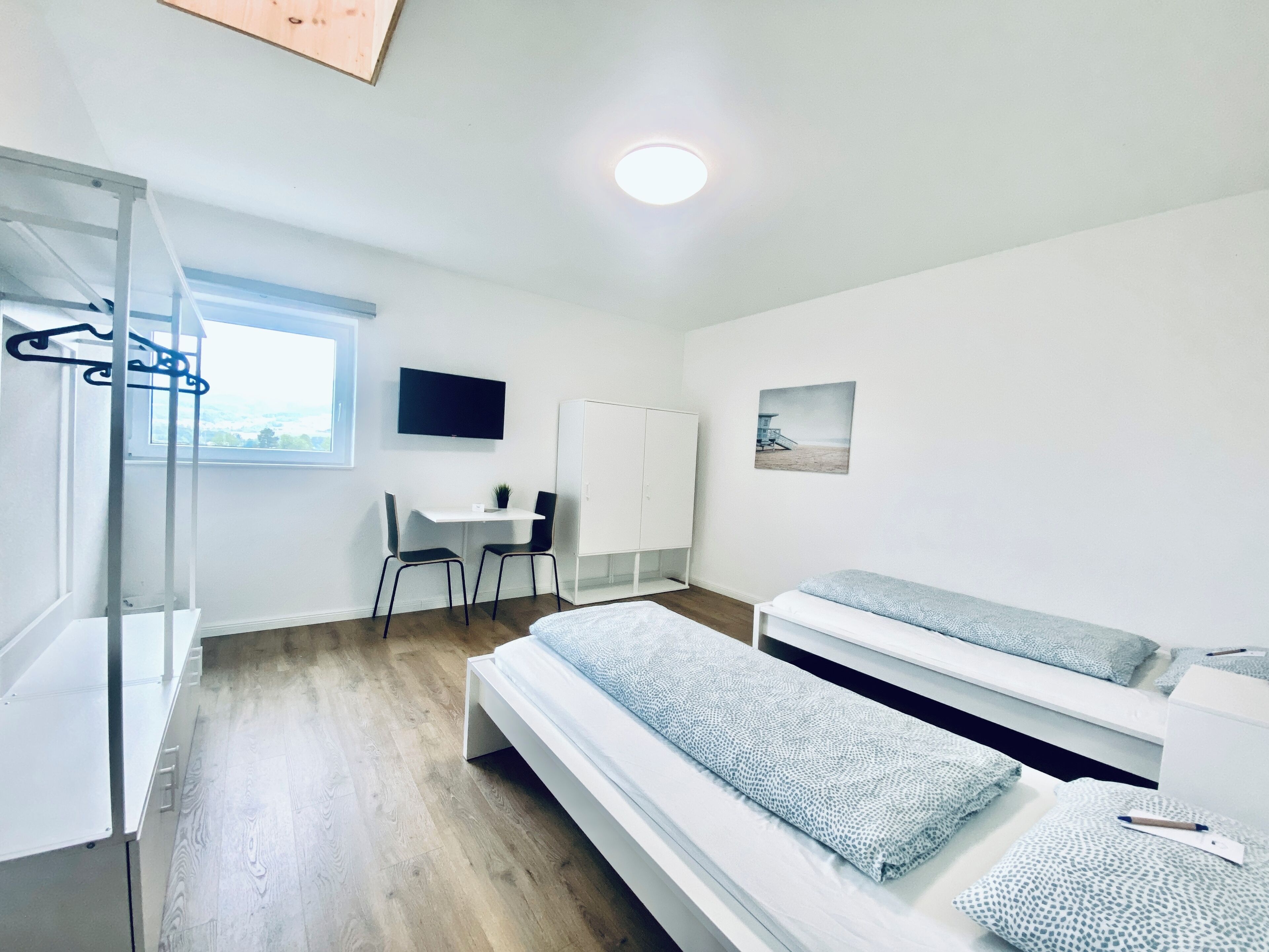 A bedroom with two beds, a desk, a chair, a wardrobe, and a TV.
