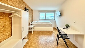 Une chambre à coucher avec un lit, un bureau, une chaise, une télévision et une fenêtre.