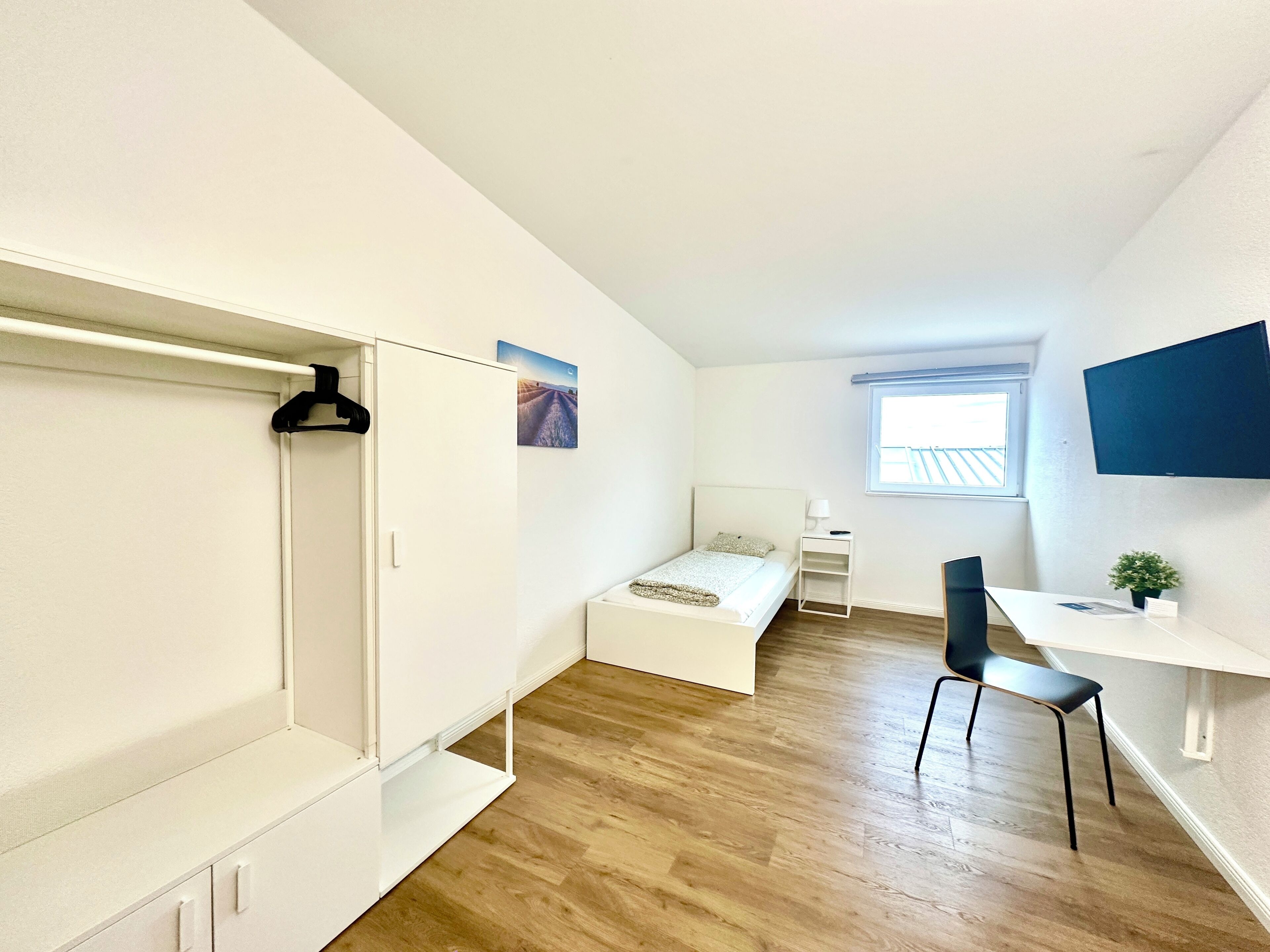 Une chambre à coucher compacte et moderne, comprenant un lit, une table de chevet et un bureau avec une chaise.