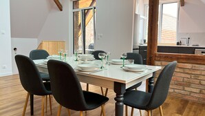 Un coin repas avec une table blanche dressée pour quatre personnes, des chaises noires et un mur en briques.