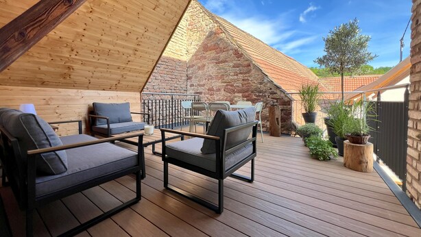 Une terrasse extérieure en bois, dotée d’un espace pour s’asseoir et d’un mur en pierre en arrière-plan.