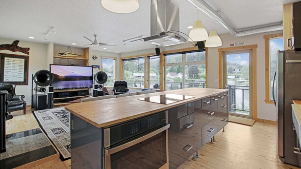 Une cuisine moderne dotée d’un îlot central, d’appareils électroménagers intégrés et de grandes fenêtres offrant une vue sur l’extérieur.