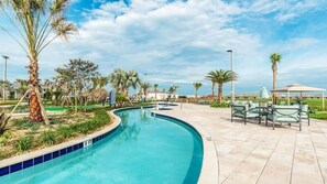 Piscina de borde curvo, rodeada de palmeras y un patio con mobiliario exterior.