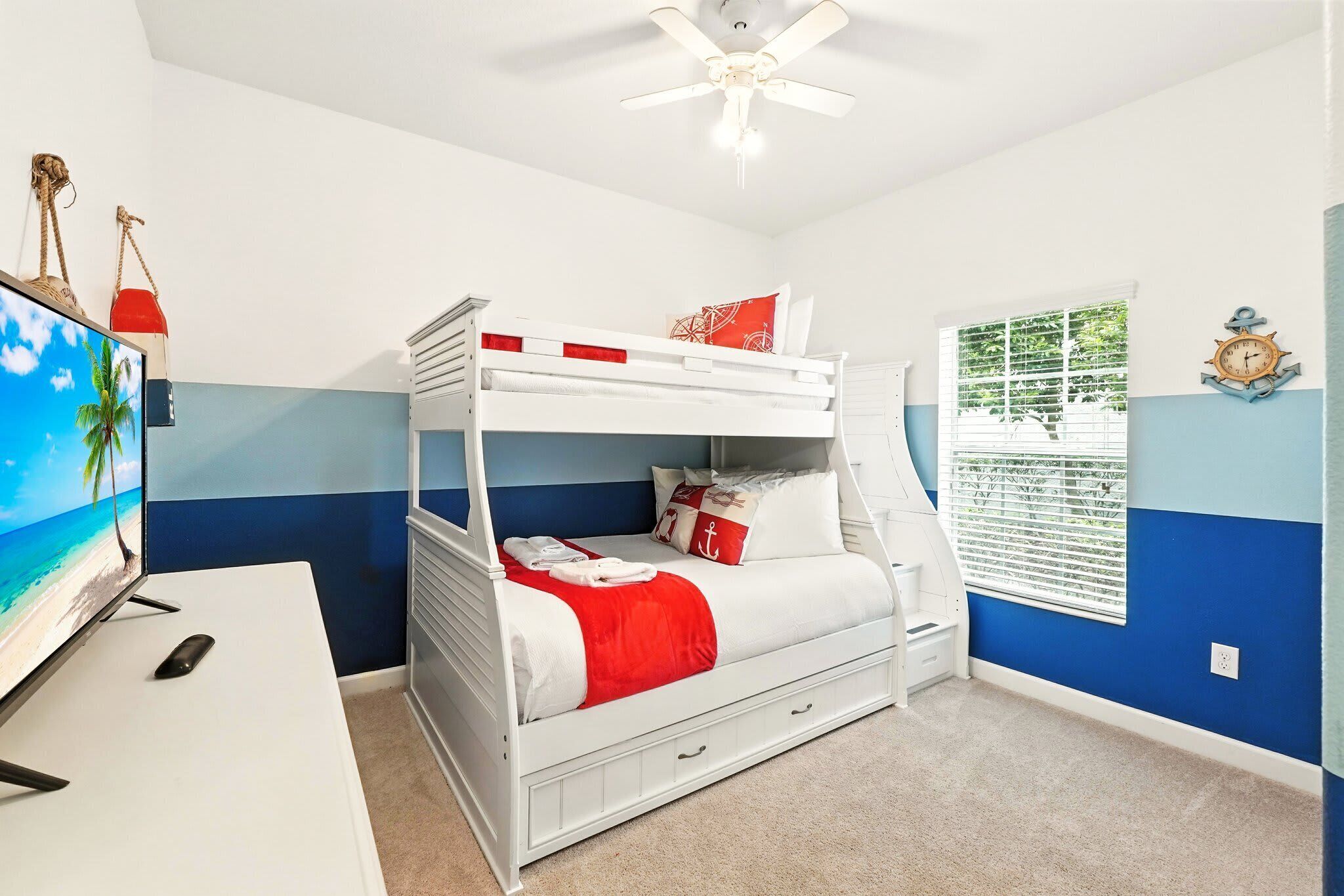 A bunk bed with a TV on a desk, a ceiling fan, and a window with blinds.