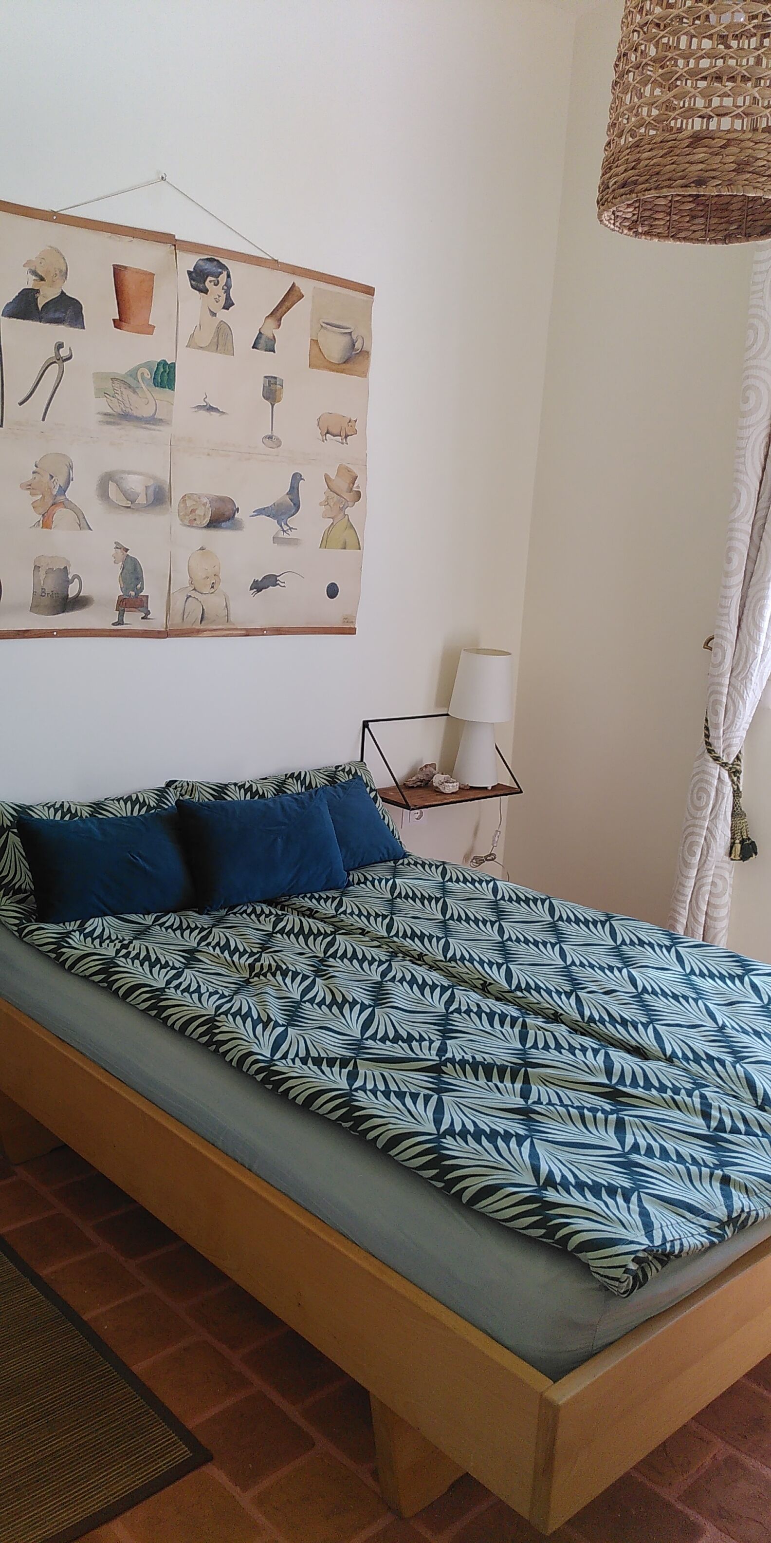 Een bed met een gebedruid sprei, een nachtkastje met een lamp, en een muur met een fotocollage.