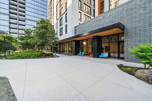 A modern building with a glass facade, outdoor seating area, and a landscaped courtyard. - New 4 King Bed / Family Ready Apartment (Chicago)