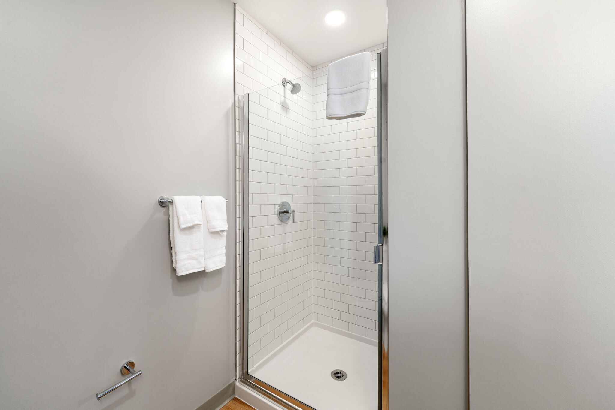 A modern bathroom with a glass shower enclosure, white tiled walls, and a visible towel rack.