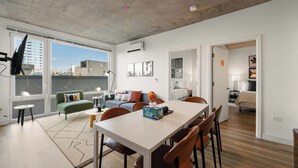 Un appartement moderne comprenant un coin repas, un salon avec un canapé et un fauteuil vert, et une chambre à coucher visible à travers une porte ouverte.