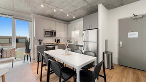 A modern kitchen with white cabinets, stainless steel appliances, and a dining area with a white table and black chairs. - Bright 3BR Stylish Apartment Near North Ave Shops (Chicago)