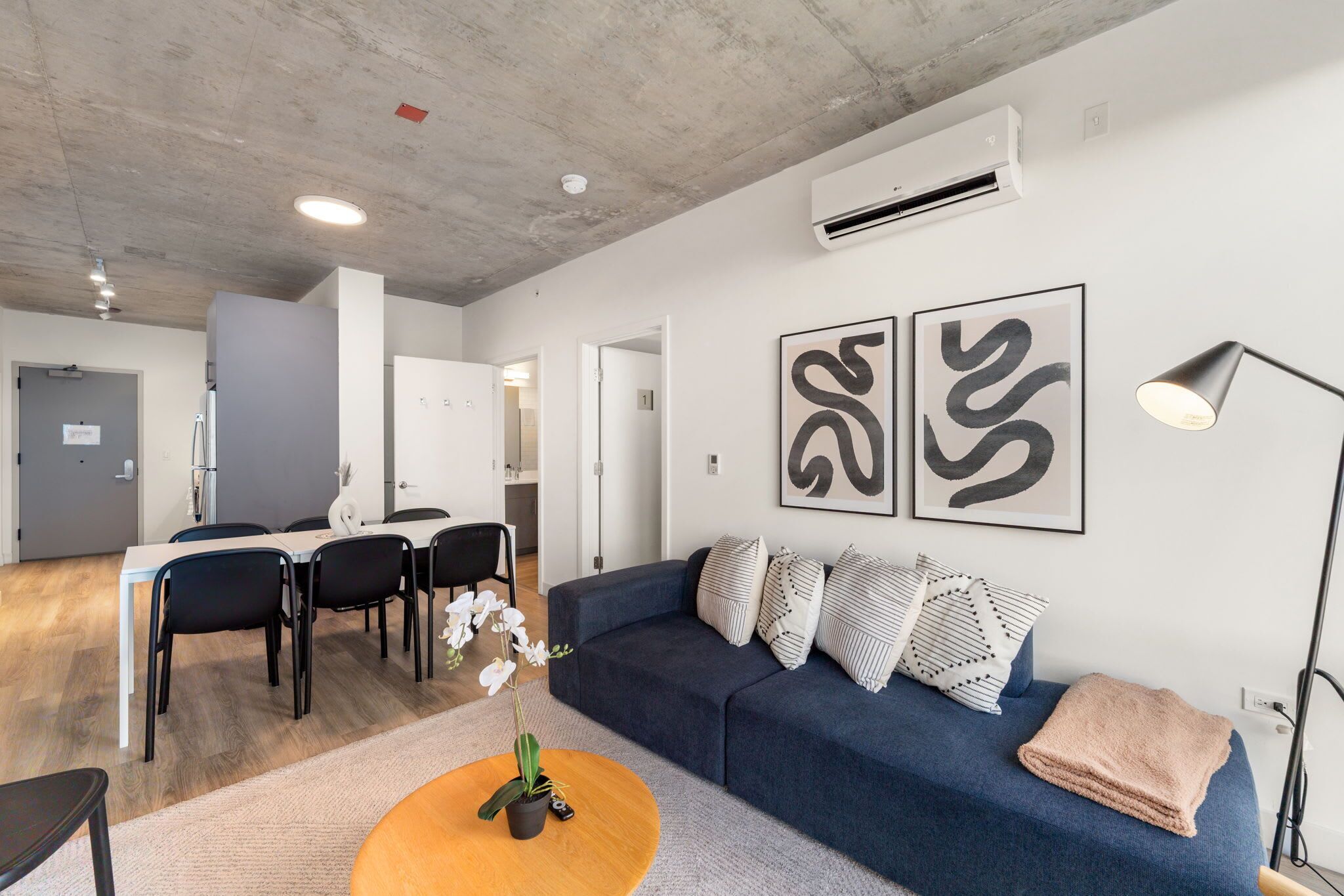 A modern living room with a blue sofa, a round coffee table, and a dining area with a white table and black chairs.