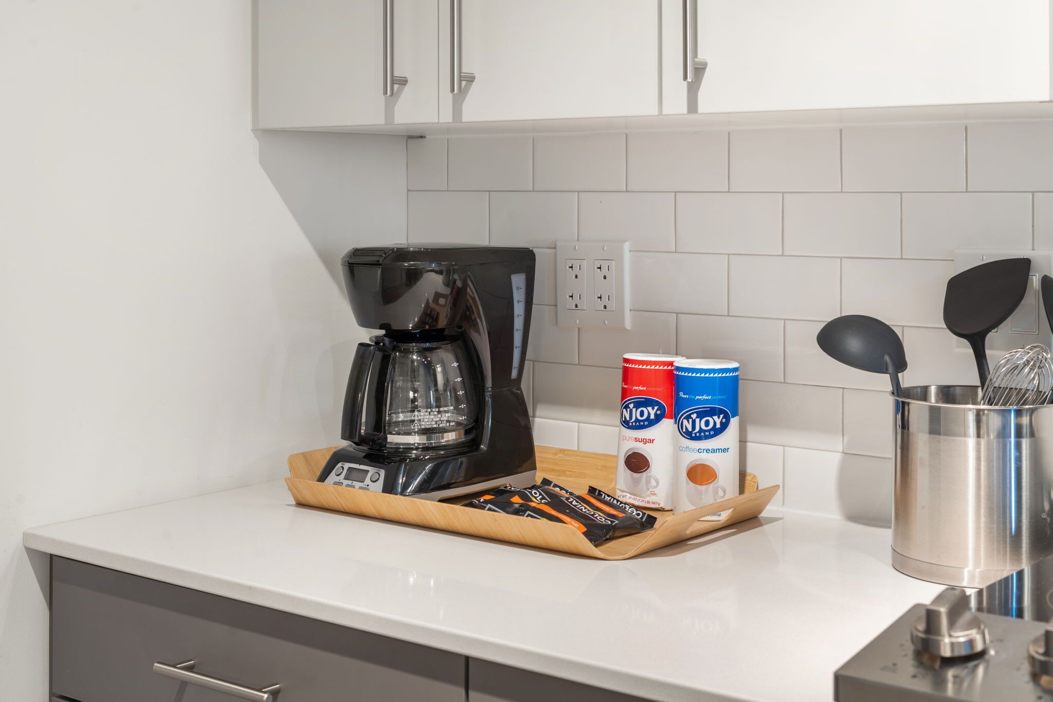 A kitchen counter with a coffee maker, a tray of coffee pods, and two Njoy coffee creamer cans.