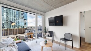 A modern living room with a large window, a flat-screen TV, a sofa, a coffee table, and two chairs. - 3BR Apartment Near Clybourn Corridor & Old Town (Chicago)