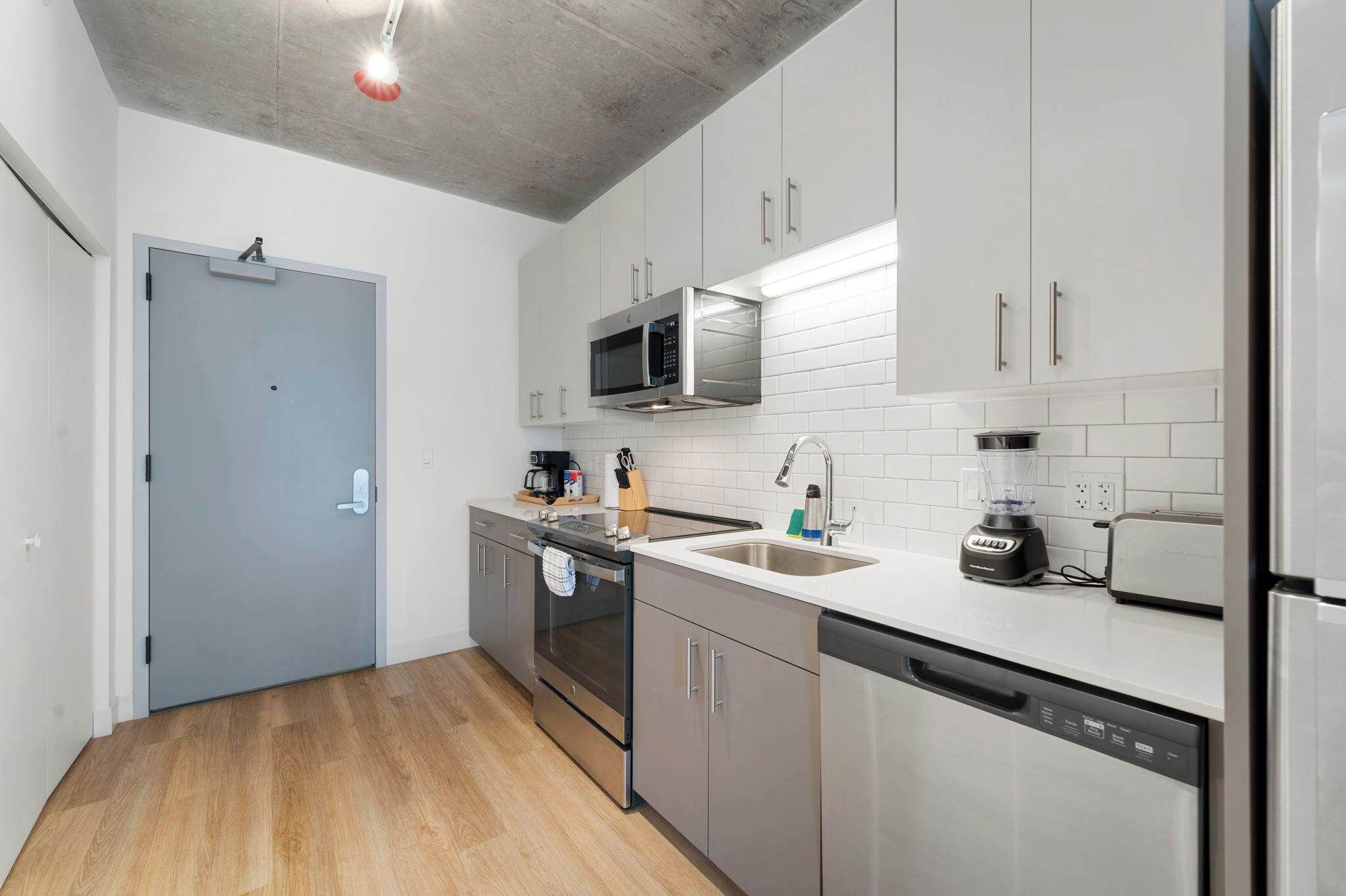 Une cuisine moderne dotée d’appareils électroménagers en acier inoxydable, de meubles blancs et d’un plancher en bois.