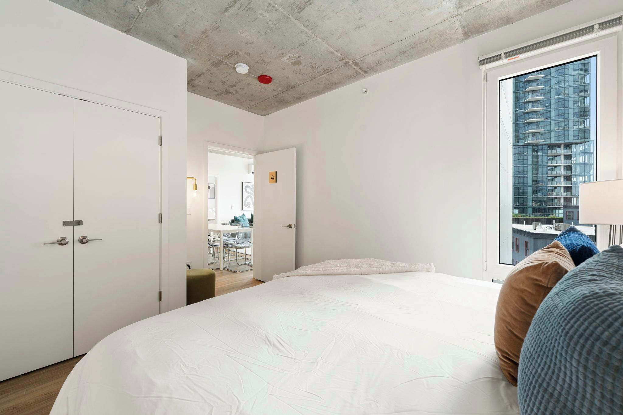 Une chambre d’hôtel moderne avec un grand lit, une vue sur un immeuble de grande hauteur et un petit coin cuisine.