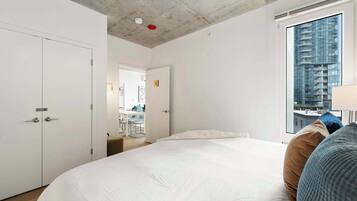 Une chambre d’hôtel moderne avec un grand lit, une vue sur un immeuble de grande hauteur et un petit coin cuisine.