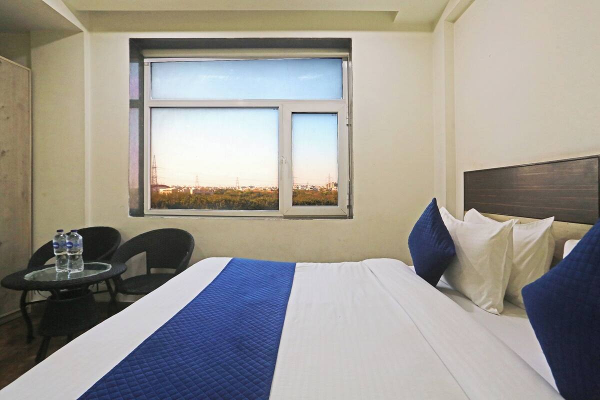 Habitación de hotel con cama, ventana con vistas a la ciudad, una mesita con dos botellas de agua y dos sillas.