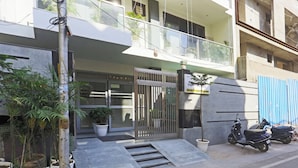 Un edificio moderno con entrada protegida, plantas en macetas y una moto estacionada afuera.