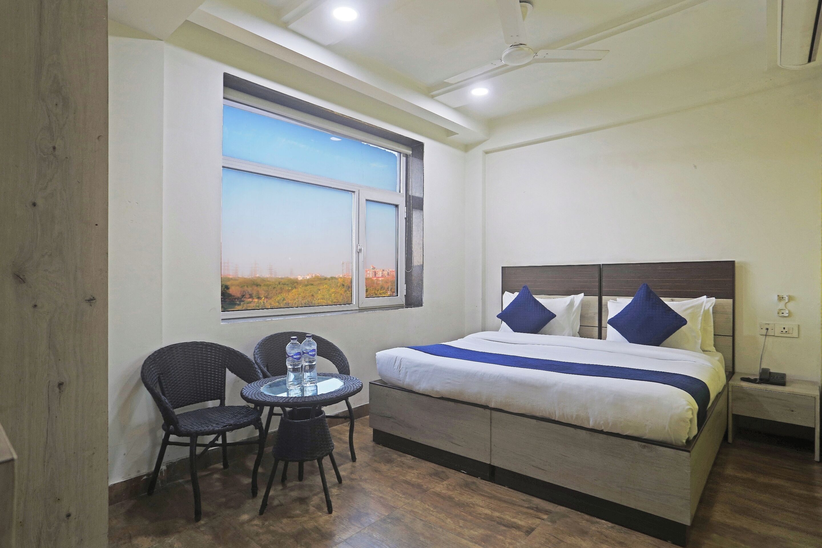 Une chambre d’hôtel avec un lit, une table et des chaises, une fenêtre donnant sur un paysage agréable et un ventilateur de plafond.