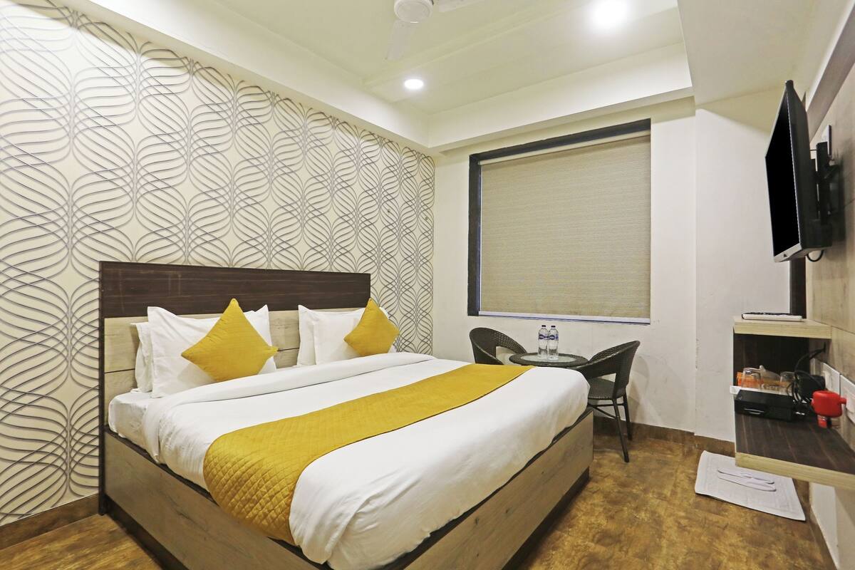 Habitación de hotel con cama, escritorio, silla, televisor y ventana con persianas.