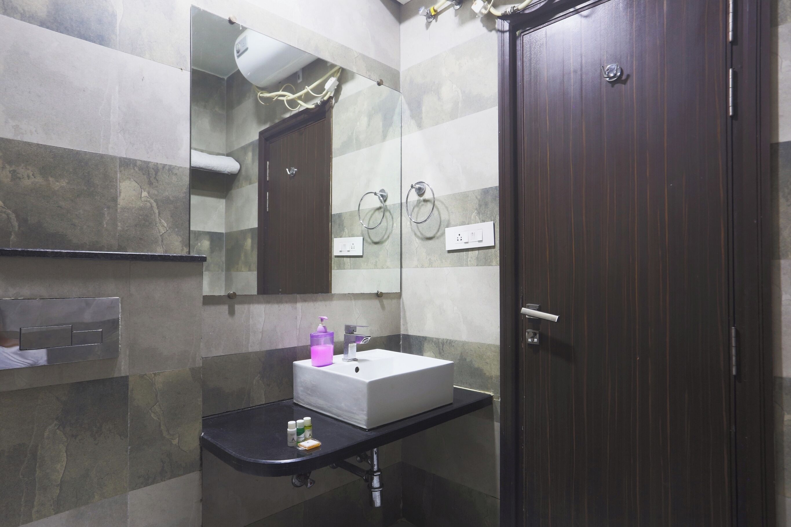 Une salle de bain avec un lavabo blanc, une porte en bois foncé et un miroir au-dessus du lavabo.