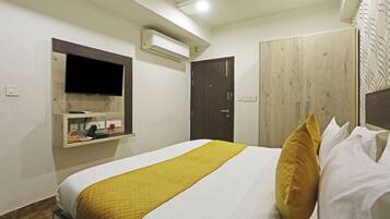 A neatly made bed with a white and yellow bedspread, a wooden wardrobe, a mounted television, and an air conditioning unit on the wall.