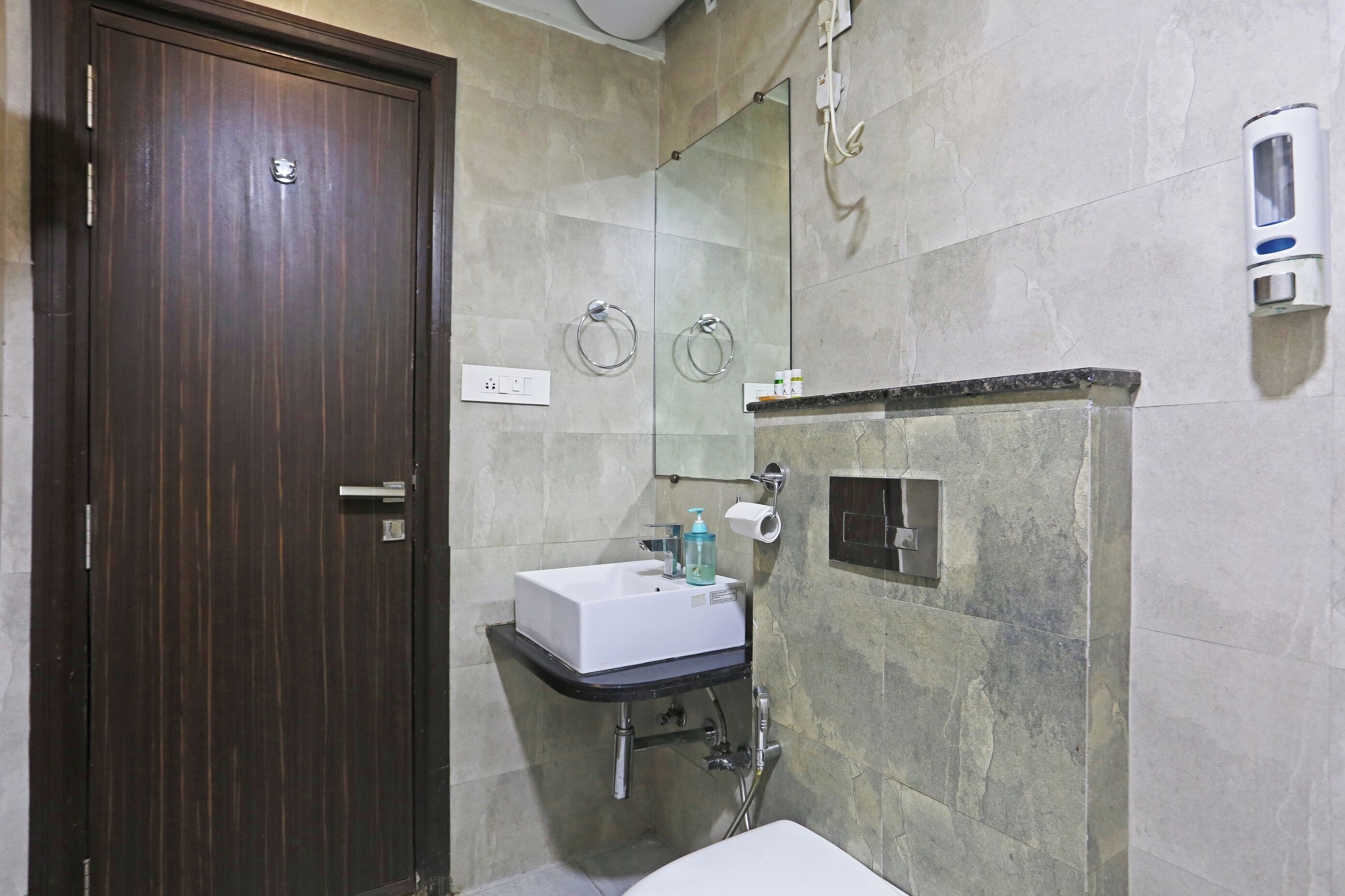 Un bagno con una porta in legno scuro, un lavabo bianco con un dispenser di sapone, uno specchio e una zona doccia.