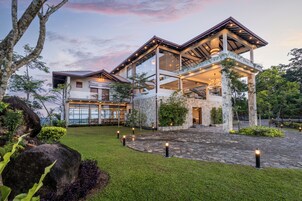 A modern two-story house with a stone facade, large windows, and a spacious front yard with a stone pathway and greenery.