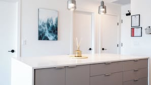 Une salle de bain moderne avec un meuble-lavabo blanc, deux lampes suspendues, une œuvre d’art encadrée et un petit vase décoratif.