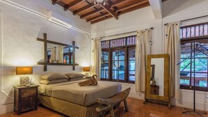 A bedroom with a large bed, a wooden headboard, a nightstand, a mirror, and a window with curtains.