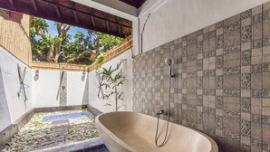 A spa area with a freestanding bathtub, a small pool with pebbles, and a tiled wall with a geometric pattern.
