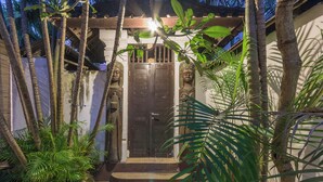 A traditional entrance with a dark wooden door, surrounded by tropical plants and a stone pathway leading to the door.