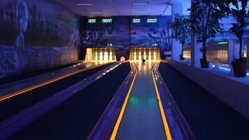 A bowling alley with multiple lanes, illuminated by overhead lights, and a mural on the wall.