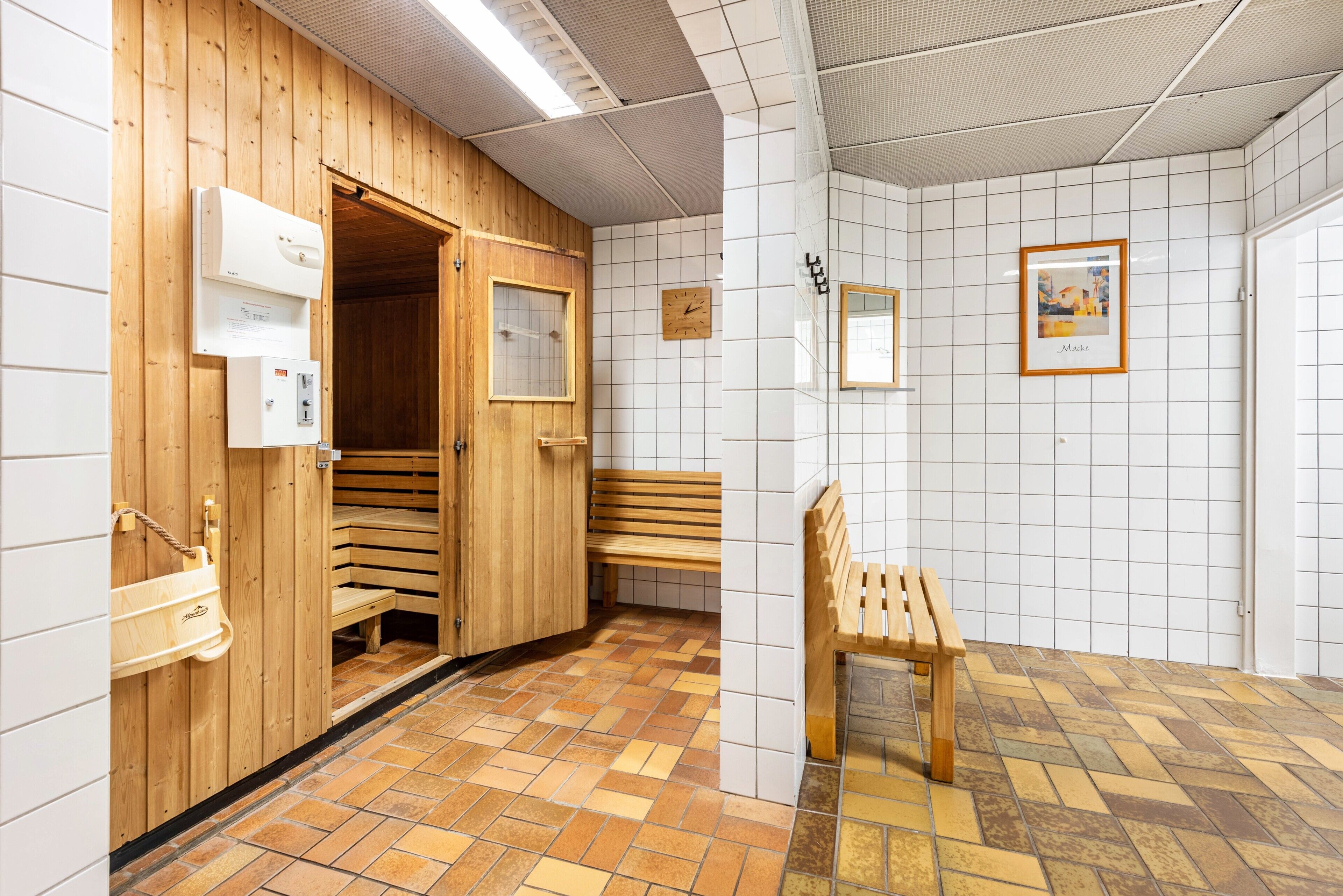 Una sauna con panche in legno, una panca esterna e una parete rivestita di piastrelle con un orologio e un quadro incorniciato.