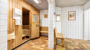 Una sauna con panche in legno, una panca esterna e una parete rivestita di piastrelle con un orologio e un quadro incorniciato.