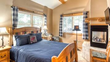 A cozy bedroom with a bed, bedside tables, a lamp, a fireplace, and windows with curtains.