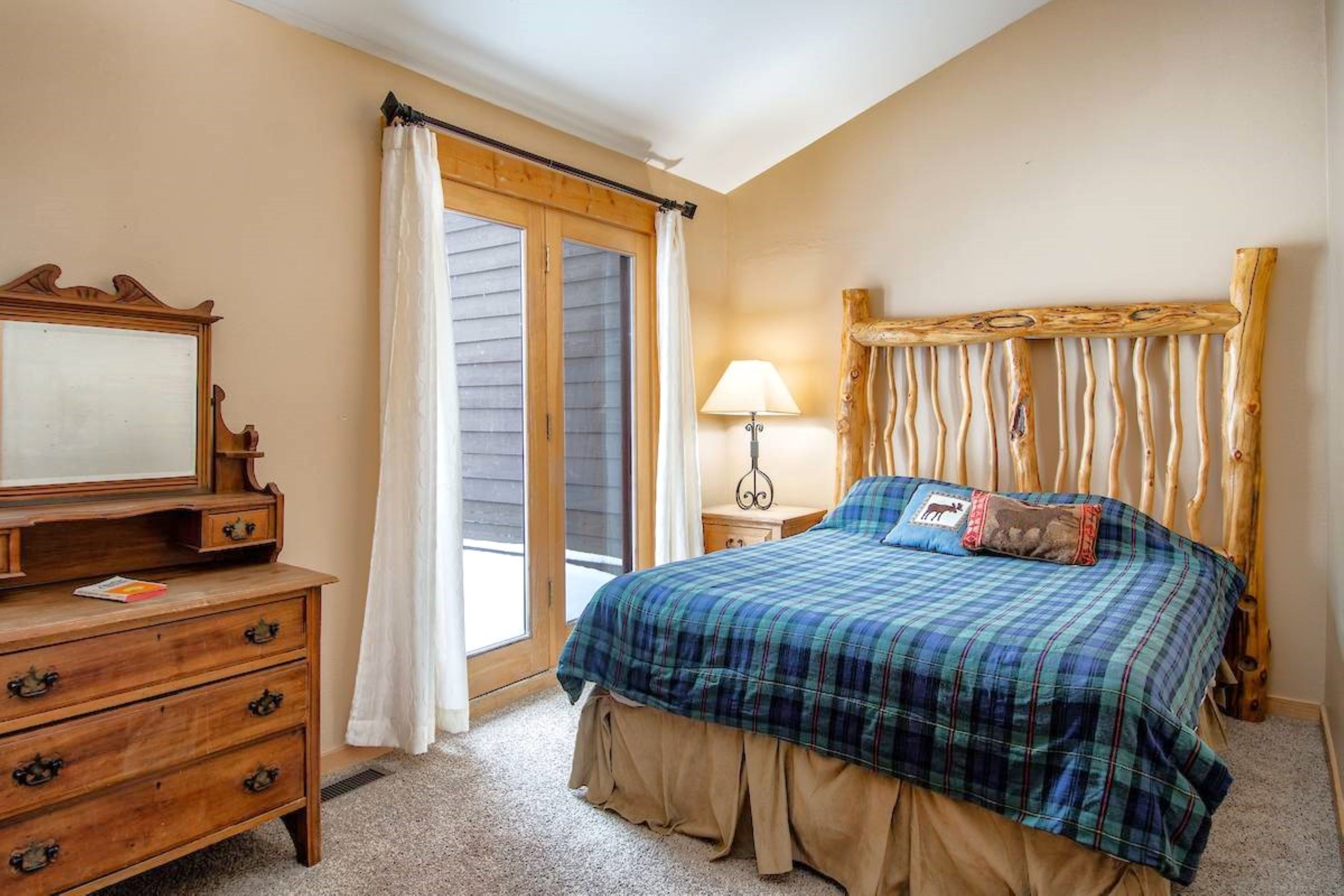 A bedroom with a bed, a dresser, a nightstand, a lamp, and a window with curtains.