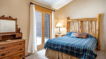 A bedroom with a bed, a dresser, a nightstand, a lamp, and a window with curtains.