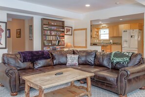 A living room with a brown leather sofa, a wooden coffee table, and a bookshelf filled with books. - Mountain Meadow Lodge • Dog-Friendly • Hot Tub (Frisco)