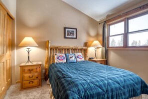 A bedroom with a bed, two bedside tables, a wooden headboard, a window, and a wall-mounted picture.