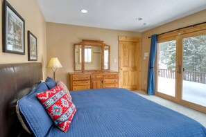 A bedroom with a large bed, a dresser, a mirror, and a sliding glass door leading to a balcony.