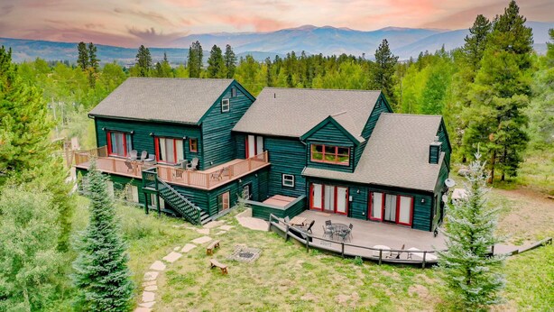 A large, two-story log cabin with a deck and outdoor seating area, surrounded by forest and mountains. - Mountain Meadow Lodge • Dog-Friendly • Hot Tub (Frisco)