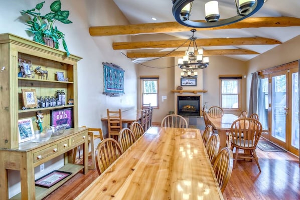 A dining area with a wooden table and chairs, a fireplace, and a bookshelf with various items.
