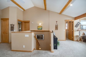 A spacious room with high ceilings, wooden beams, a built-in bench, a staircase, and a small table with a lamp.
