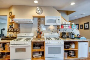 A compact kitchen with a microwave, two gas stoves, a coffee maker, and various kitchen utensils.