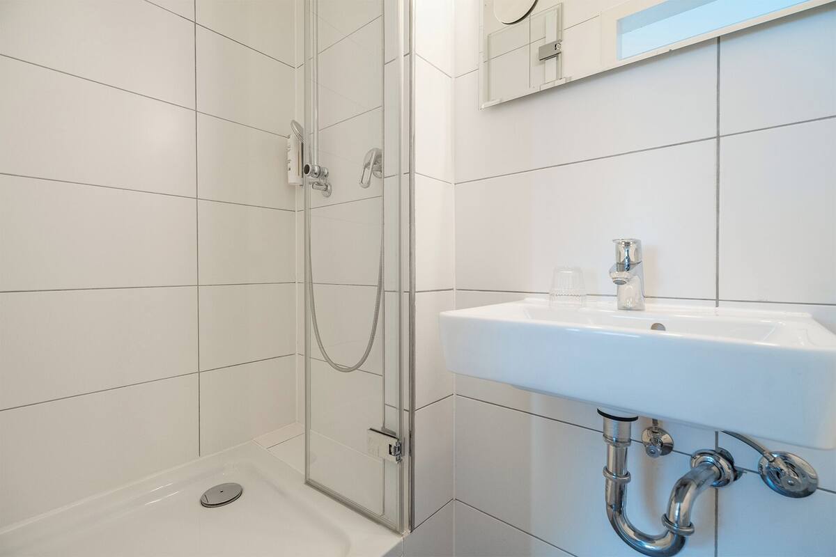 Un bany modern amb un espai de banyera de vidre, un lavabo blanc i un mirall sobre el lavabo.