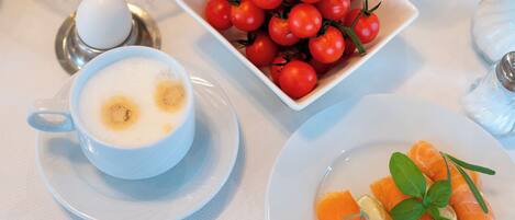 Un desayuno con una taza de café, un bol de tomates cherry y un plato de salmón con limón y hierbas.