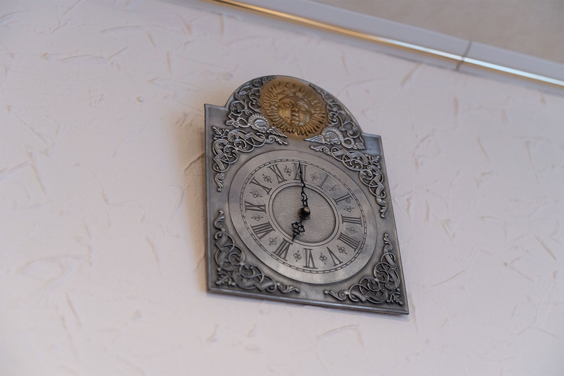 A wall-mounted clock with ornate designs and Roman numerals.