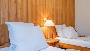 A room with two beds, a wooden wall, and a bedside lamp.